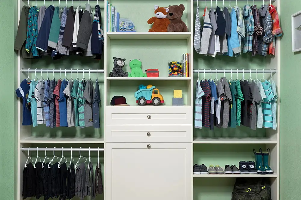 Kids’ closet with double hanging, white drawers and toy shelves by Famille Closets