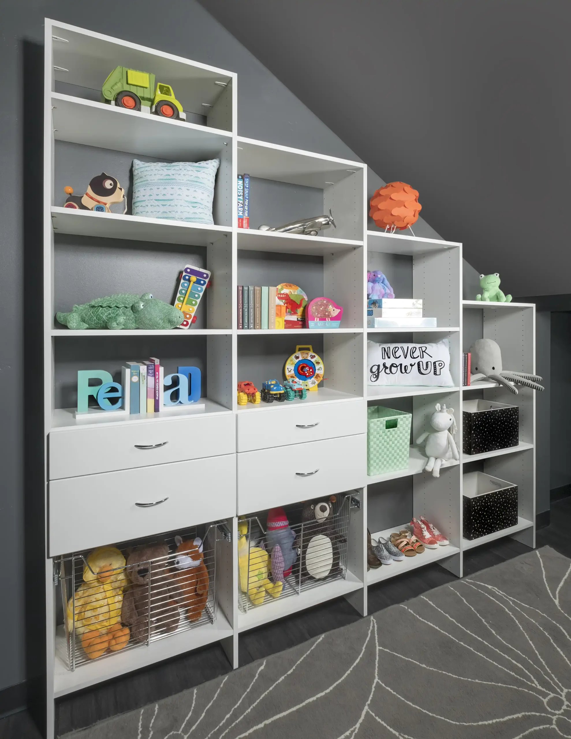Kids’ storage wall with open shelving, toys and bins under a sloped ceiling by Famille Closets