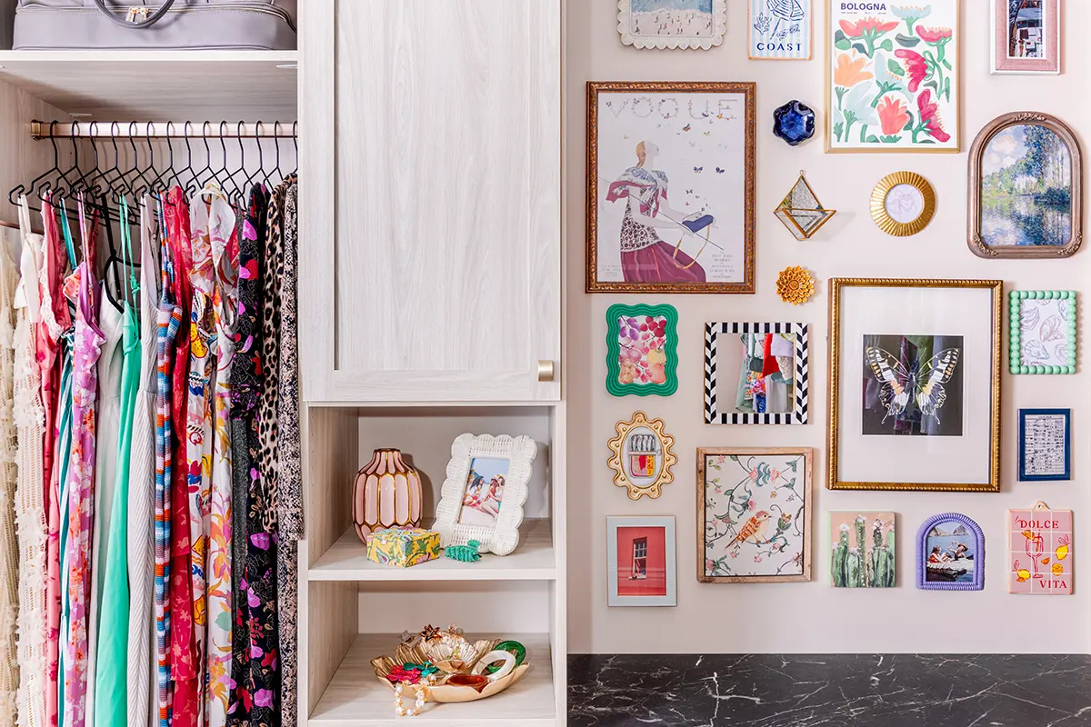 Reach-in closet with light wood-grain shaker cabinets, open shelving and hanging rod beside a gallery wall