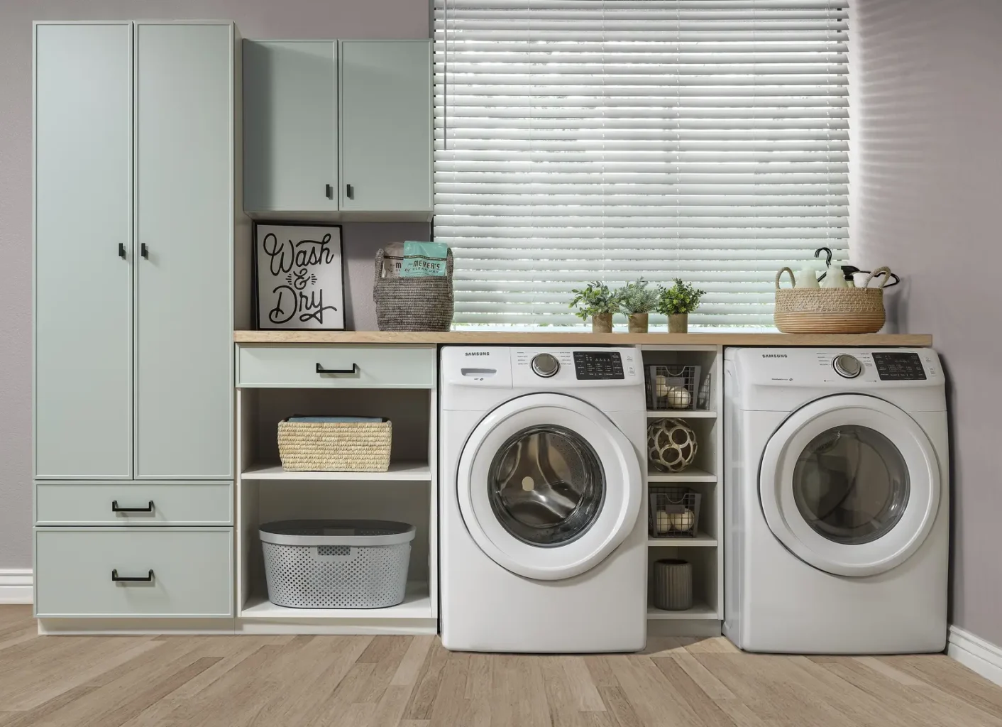 Custom laundry room with sage-green cabinets, open cubbies and a countertop over the washer and dryer