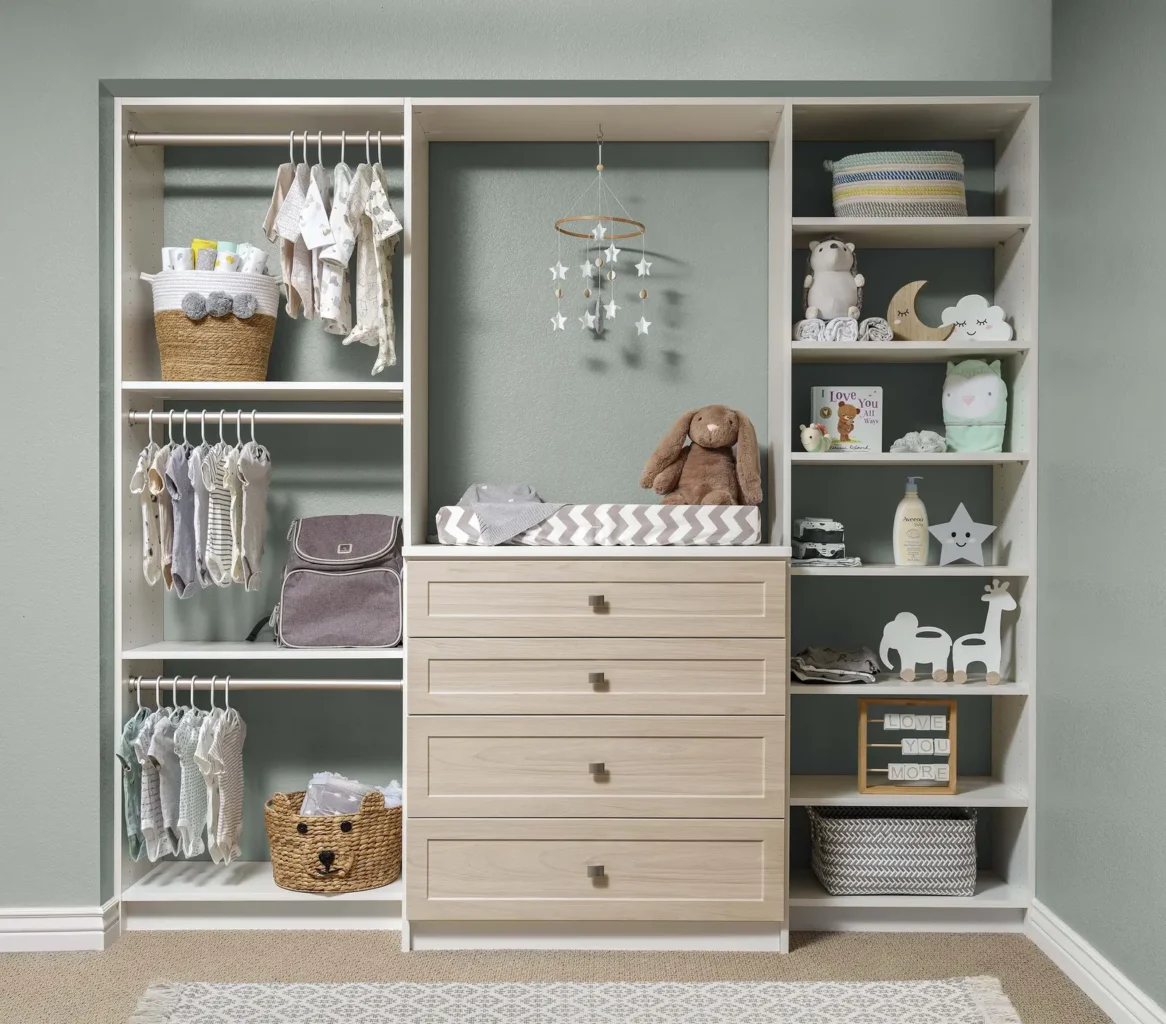 Nursery closet with white shelving, hanging rods and light wood drawers