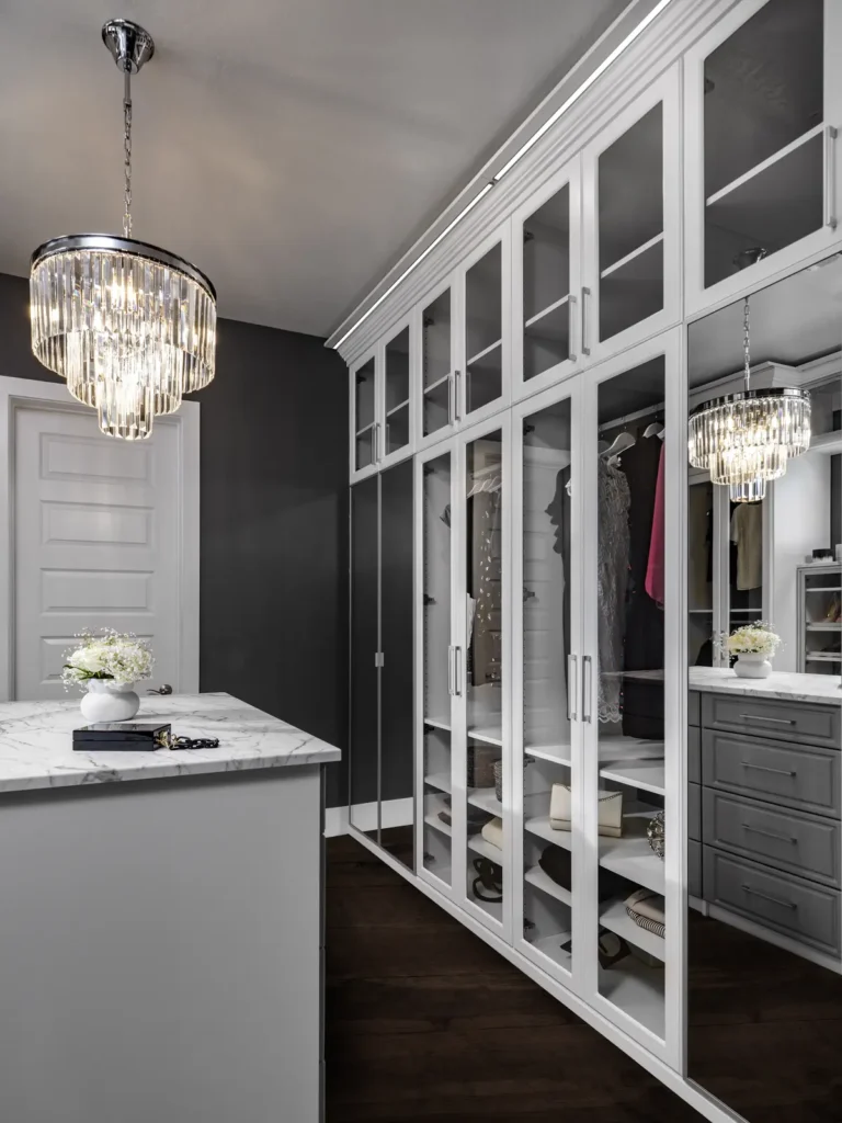 Walk-in closet with white glass-front cabinets, a centre island and crystal chandeliers