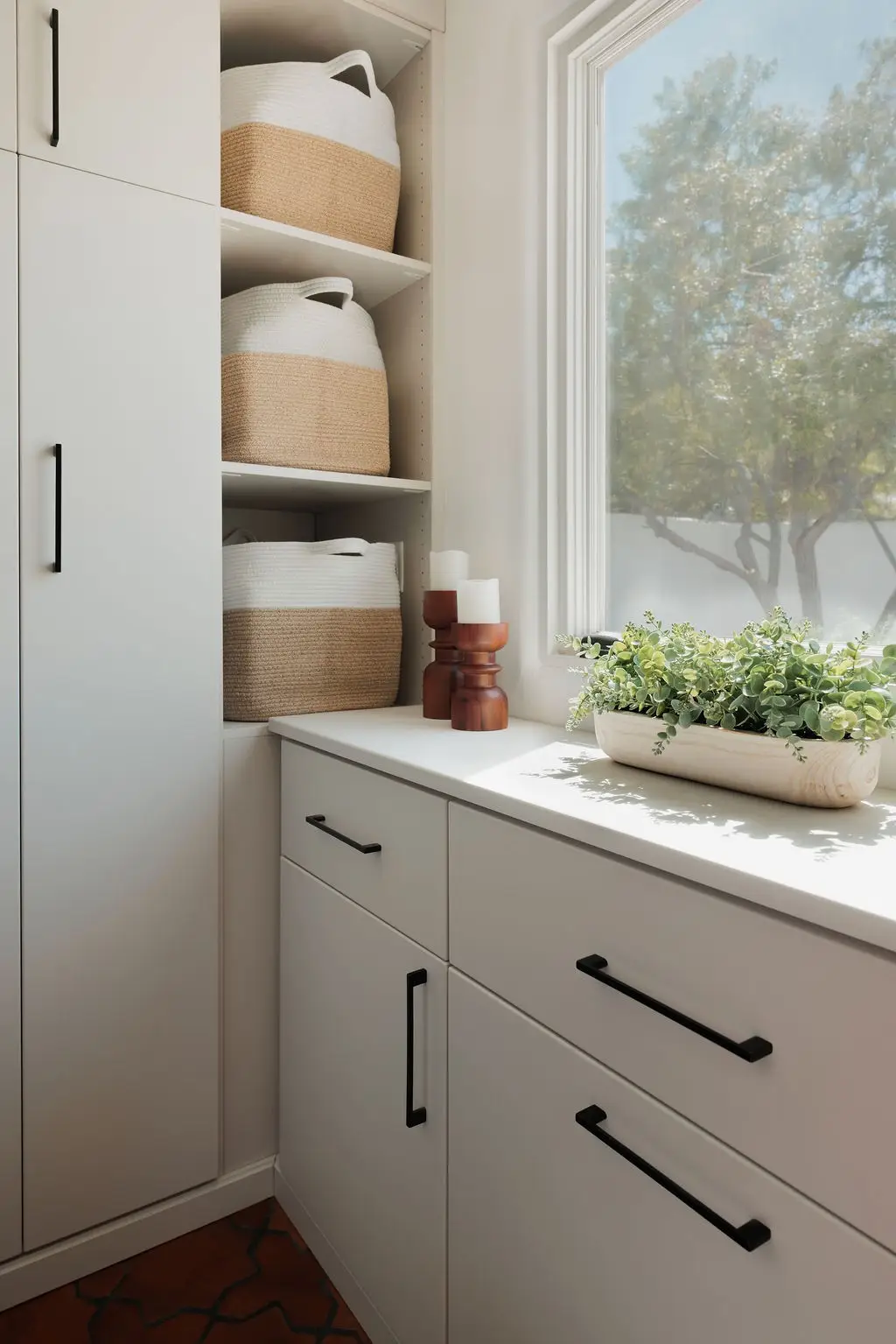 Vintage finish laundry room cabinets and drawers with black pulls beside a window