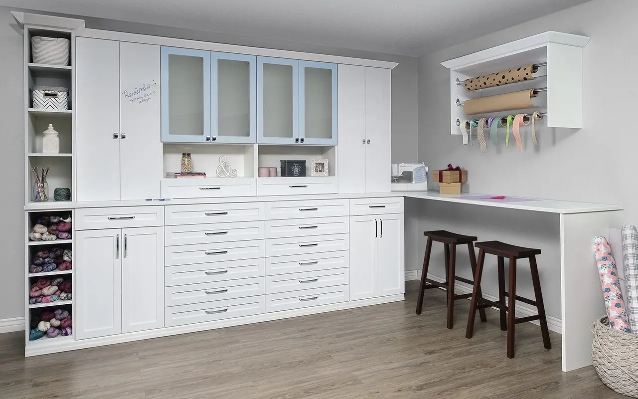 White craft room with drawer banks, glass-front cabinets and a work counter by Famille Closets