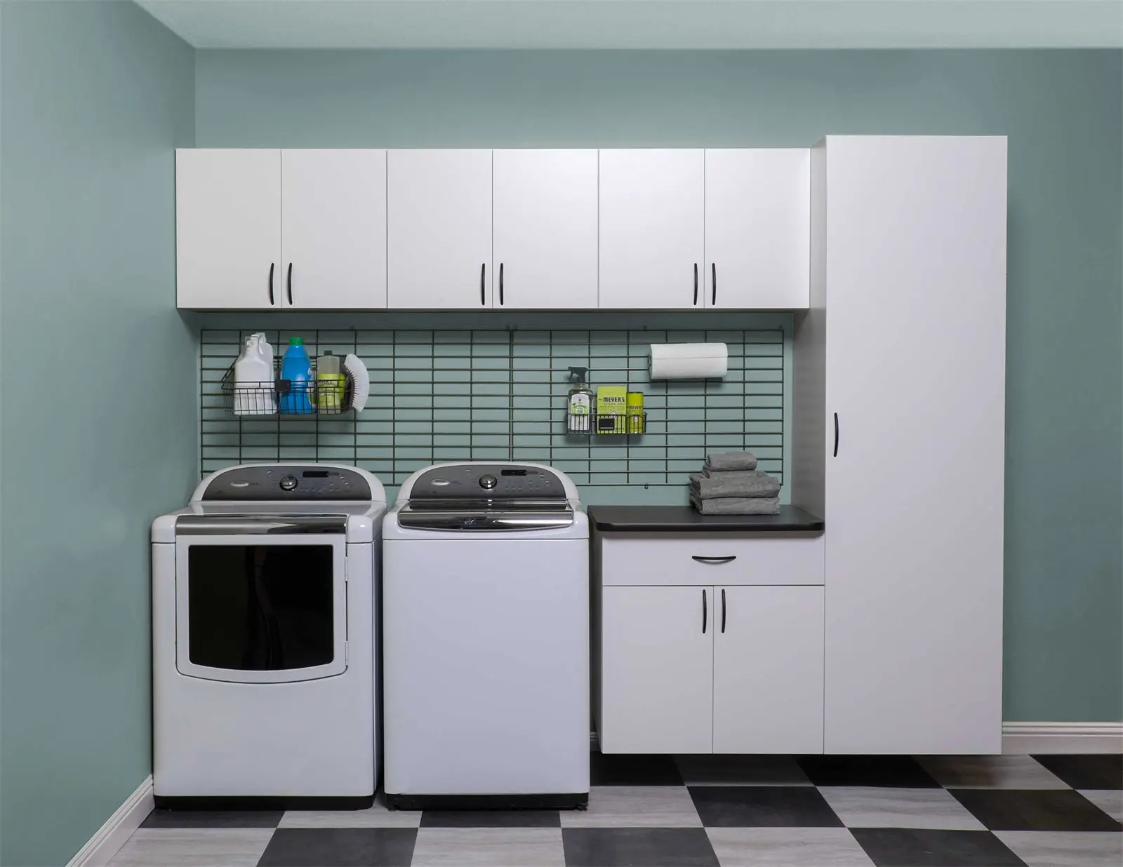 White laundry room cabinets with a wall rack and counter beside the washer and dryer by Famille Closets