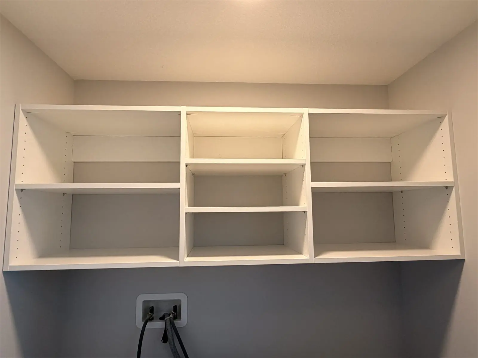 White open shelving installed above a laundry hook-up by Famille Closets